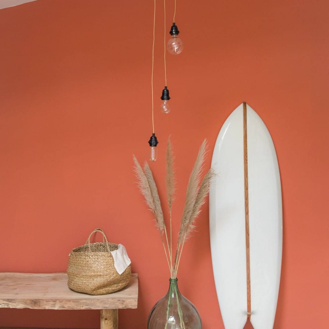 Pièce avec un mur orange une planche de surf blanche et une suspension Hang 3 fils Hoopzi